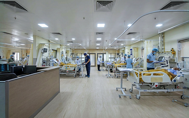 A well-equipped hospital room with patients in beds, medical staff attending to them, and advanced monitoring equipment visible. The clean, organized space highlights a modern healthcare facility.