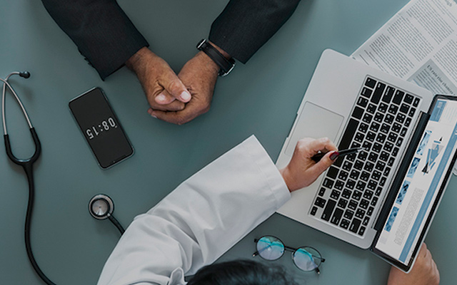Doctor and patient discussing medical issues using a laptop and phone in a healthcare setting